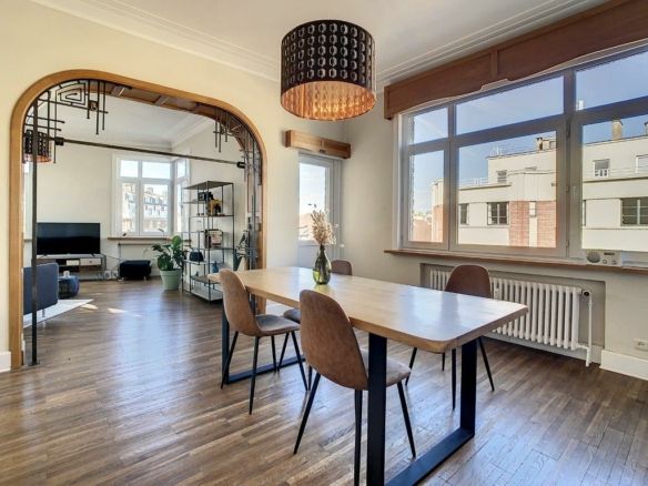 Salle à manger moderne avec table en bois, éclairage design, lumière naturelle et décoration végétale élégante.