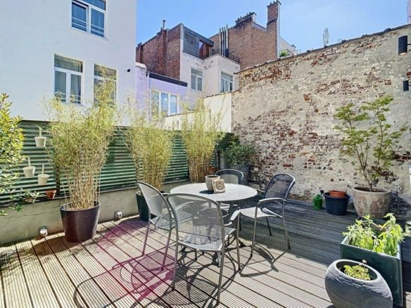 Terrasse urbaine ensoleillée avec mobilier moderne, plantes vertes et mur en briques.