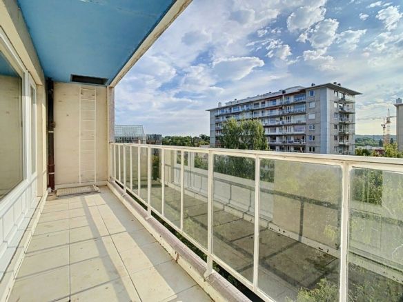 Balcon lumineux avec vue urbaine, arbres, ciel bleu et nuages blancs, idéal pour la détente.