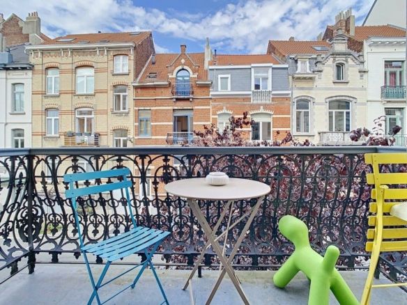 Balcon urbain coloré avec mobilier, vue pastel, ciel bleu, plantes, ambiance détendue et conviviale.