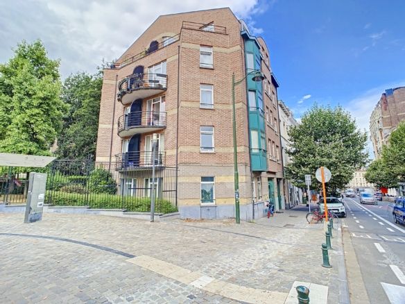 Immeuble résidentiel moderne avec balcons, jardins verts, situé à un coin de rue en environnement urbain.