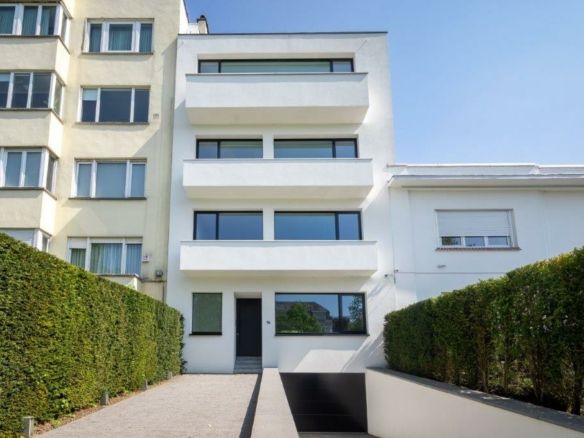 Villa moderne à Bruxelles avec balcons en verre, façade blanche et jardins soignés.