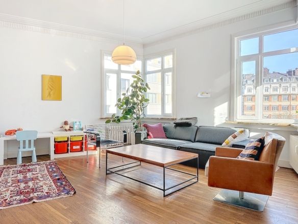 Salon lumineux avec canapé en cuir, décoration moderne et espace enfant coloré, éclairé par la lumière naturelle.