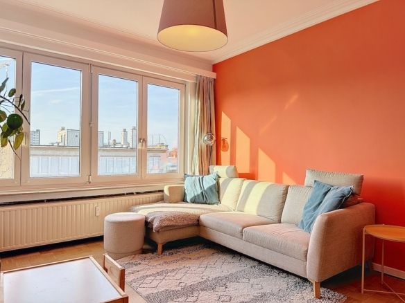 Salon moderne avec mur orange, canapé confortable, meubles en bois clair et décoration végétale.