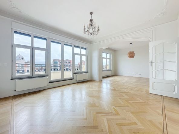 Lichte kamer met visgraatparketvloer, grote ramen, elegante kroonluchter en klassiek lijstwerk.