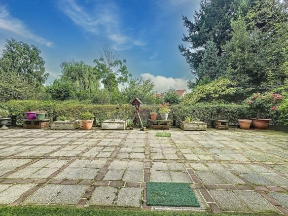 Jardin paisible avec terrasse en pierre, fleurs colorées, arbres et ambiance relaxante en plein air.