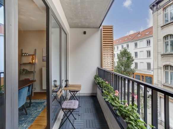 Balcon moderne avec plantes, fauteuil bleu, vue urbaine, lumière naturelle, ambiance zen et conviviale.