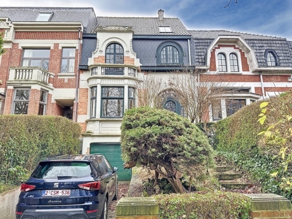 Historische villa met tuin, sierlijke ramen, pannendak, moderne zwarte auto aan de voorkant.