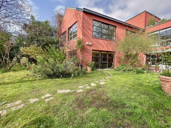 Maison moderne intégrée à la nature avec jardin luxuriant, fenêtres panoramiques et toit plat épuré.