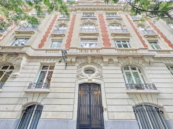 Façade élégante en pierre et brique, détails raffinés, fenêtres en fer forgé, environnement verdoyant.