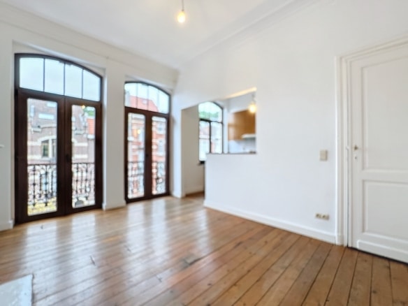 Salon lumineux avec parquet en bois, grandes fenêtres et accès à terrasse, style moderne et classique.