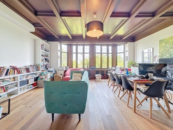Salon lumineux avec fauteuil vintage, bibliothèque, espace de travail et plantes vertes.