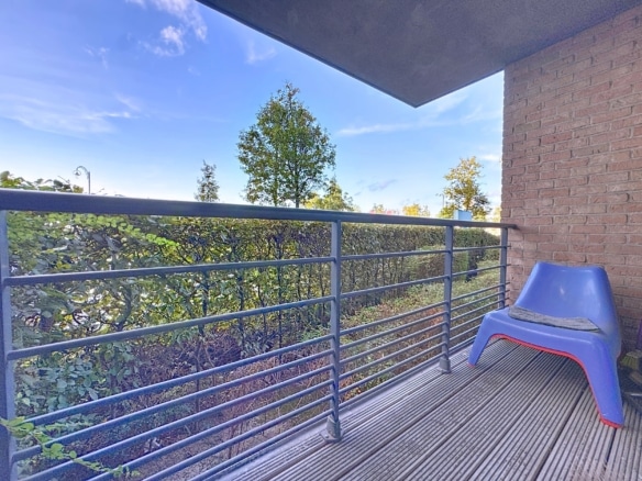 Balcon minimaliste avec fauteuil bleu, vue verdoyante, ambiance paisible et design contemporain.