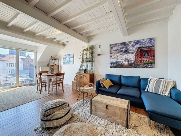 Lichte woonkamer met houten balken, blauwe bank, gezellige eethoek, plantendecoratie.