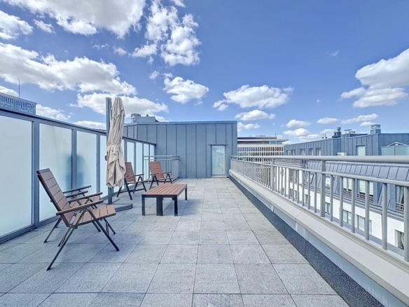 Terrasse urbaine moderne avec chaises en bois, parasol beige et vue panoramique sur la ville.