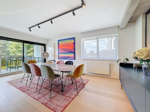 Lichte, moderne eetkamer met kleurrijk meubilair, abstracte kunstwerken en toegang tot een lommerrijk balkon.