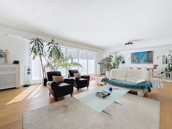 Lichte woonkamer met witte bank, zwarte fauteuils, kamerplanten en moderne eethoek.