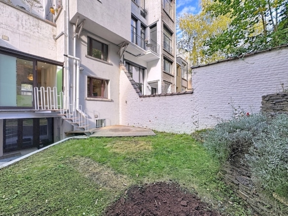 Jardin moderne avec terrasse pavée, pelouse verte, buissons et lumière naturelle.