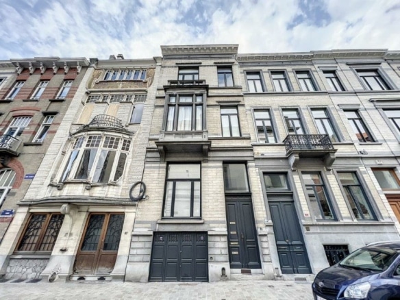 Rue pittoresque avec bâtiments en pierre, balcons, façades élégantes et ciel nuageux.