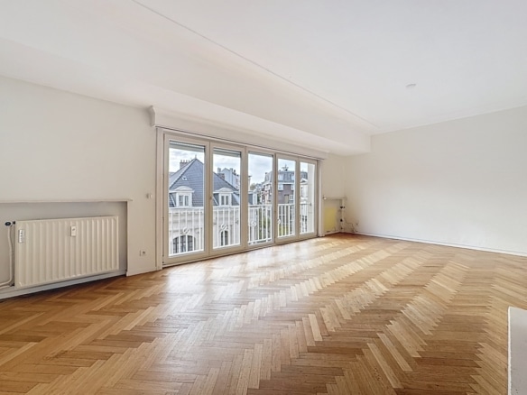 Salon lumineux avec parquet en chevrons, grandes baies vitrées et vue sur balcon.