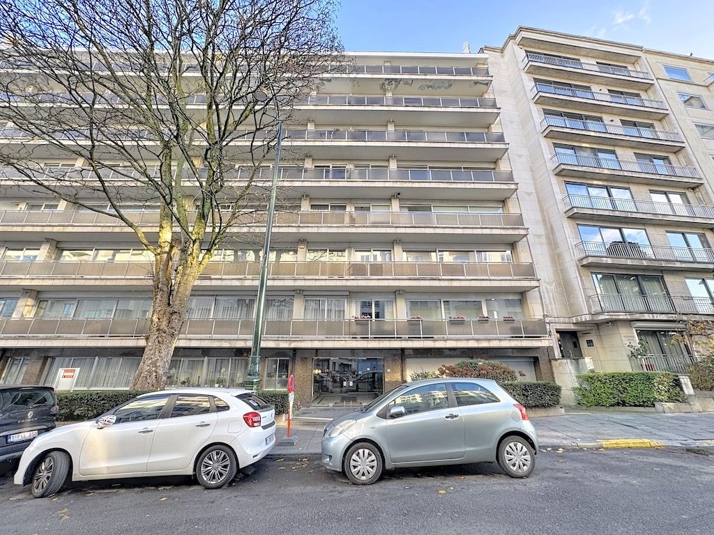 Immeuble résidentiel moderne à Bruxelles avec balcons en verre, parking et arbres dénudés.