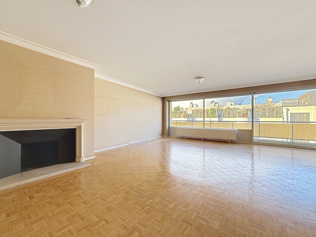 Salon lumineux avec vue panoramique sur Bruxelles, parquet, murs neutres, grande baie vitrée, espace prêt à aménager.