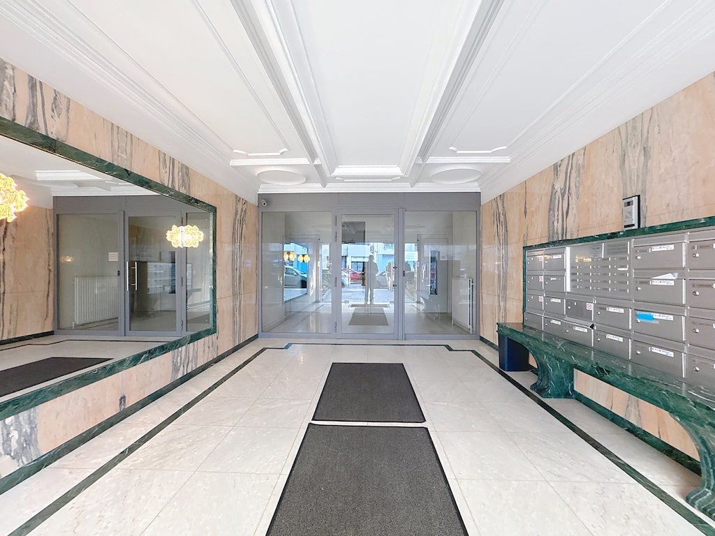 Hall d’entrée lumineux avec miroir, boîtes aux lettres, mobilier moderne et vue sur salon à Bruxelles.