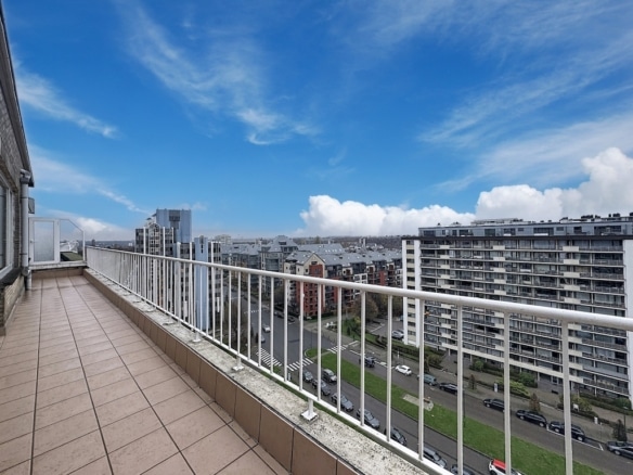 Balcon moderne avec vue sur ville, ciel bleu, bâtiments modernes et espace extérieur paisible.