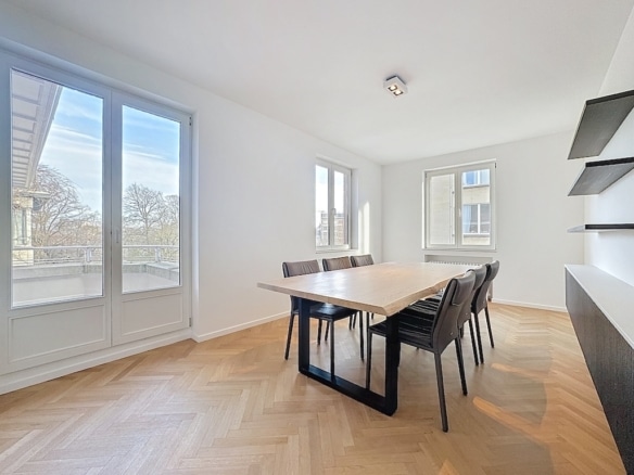 Salle à manger moderne lumineuse avec table en bois, chaises noires et grandes fenêtres.