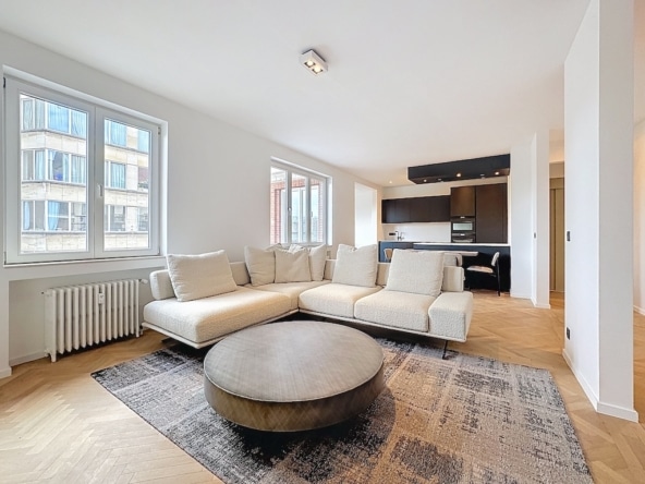 Salon lumineux avec canapé minimaliste grande baie vitrée et cuisine moderne en arrière plan