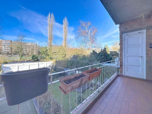 Balcon paisible avec vue sur jardin vert, ciel bleu, et balustrade blanche, idéal pour la détente.