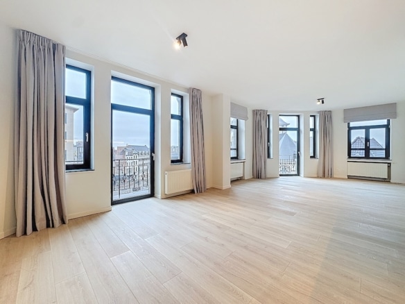 Salon lumineux avec grandes fenêtres, vue urbaine, parquet en bois clair, style moderne et épuré.