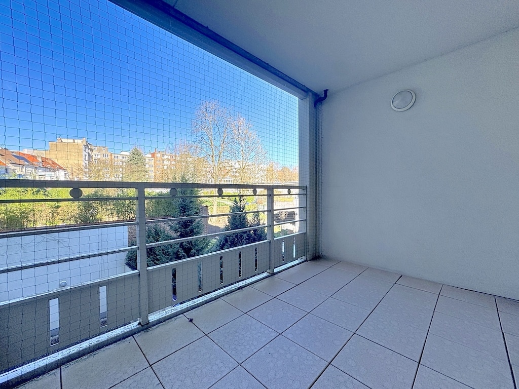 Ruim balkon met uitzicht op de stad, zwarte reling, veiligheidsnet en lichtgekleurde tegelvloer.