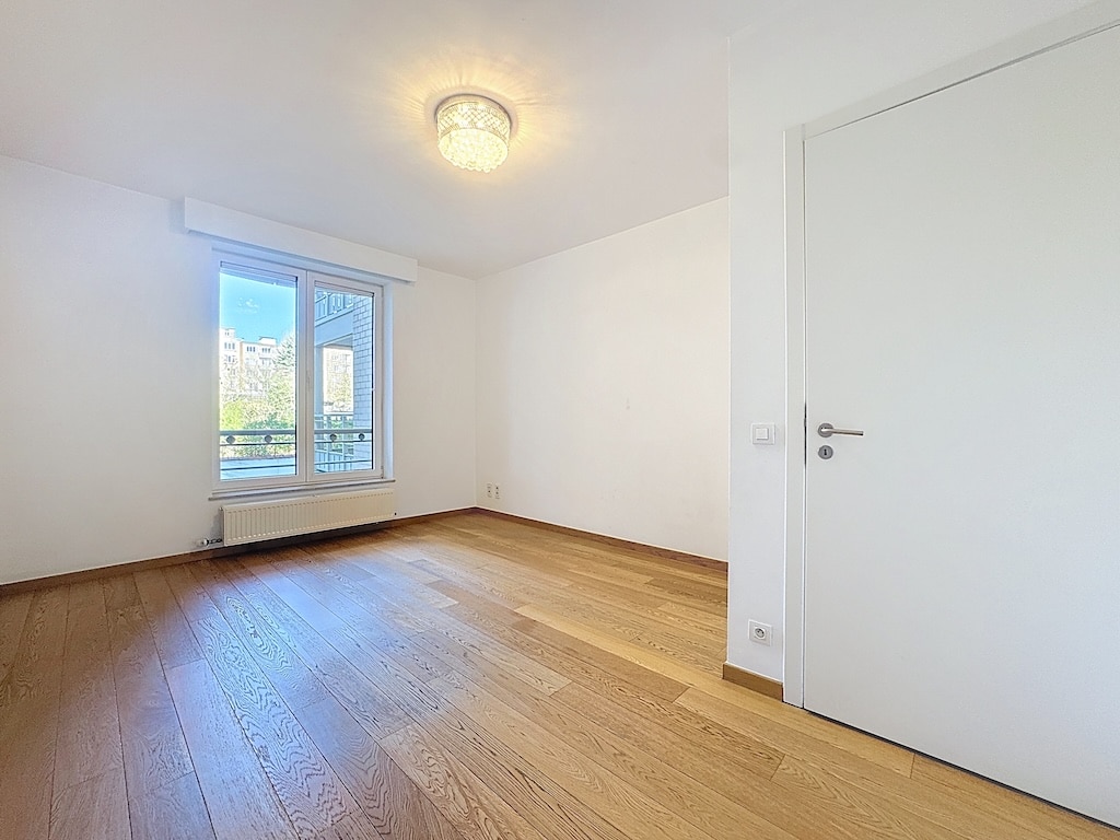 Lichte kamer met groot raam, lichte houten vloer, minimalistische stijl in Elsene.