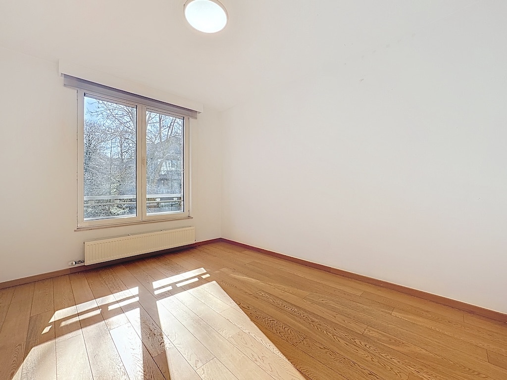 Lichte, minimalistische kamer met houten vloer, groot raam, uitzicht op de natuur in Elsene.