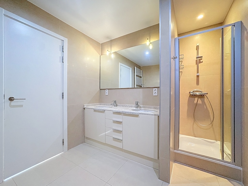 Lichte, moderne badkamer met opgeruimd uitzicht, glazen douche en wit badmeubel.