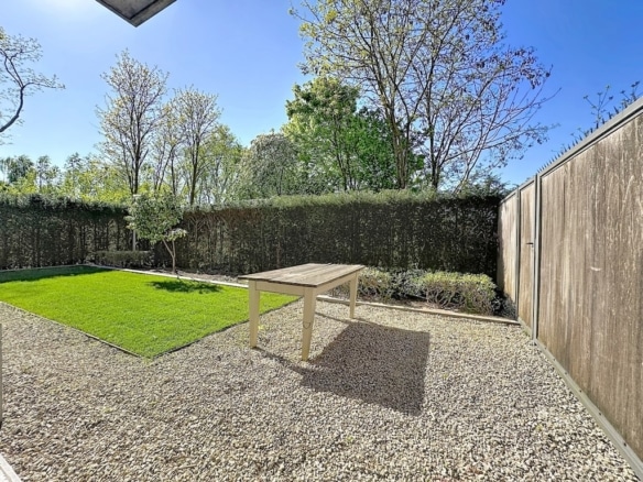 Bright enclosed garden with gravel terrace, green lawn and wooden fence