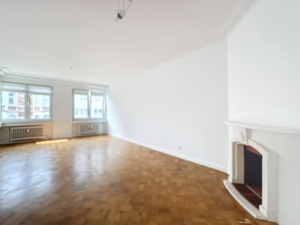 Bright living room with parquet floor, white fireplace and windows in empty apartment