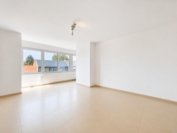 Salon lumineux vide avec grandes fenêtres carrelage beige et vue sur les toits   appartement 1 chambre  forest