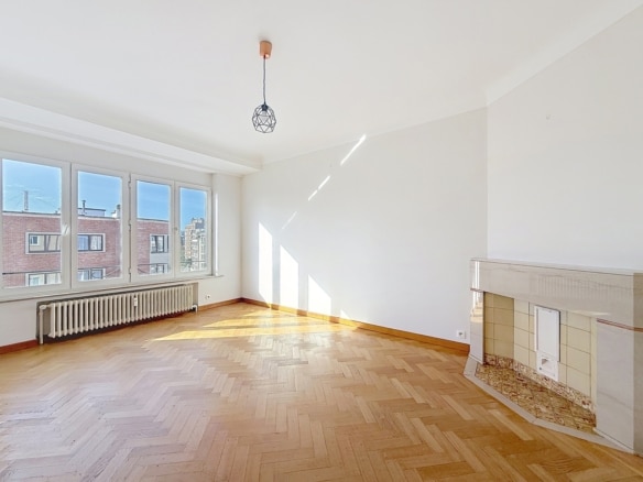 Salon lumineux avec parquet à chevrons grandes fenêtres et cheminée en pierre   appartement 1 chambre  ixelles