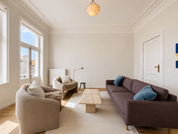 Salon dappartement lumineux avec hauts plafonds moulurés parquet clair et canapé aubergine   appartement 1 chambre  bruxelles