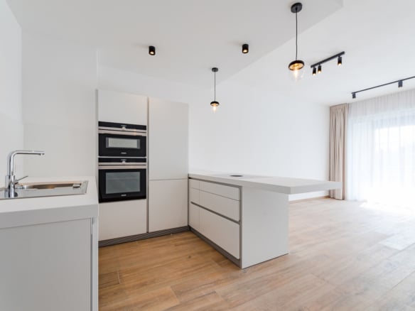 Bright white minimalist kitchen with built in ovens island and large window with sheer curtains   appartement 1 chambre  uccle