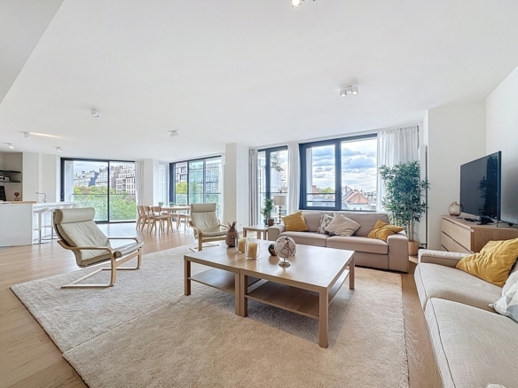 Lichte, luchtige woonkamer met beige banken, een houten salontafel en grote ramen met uitzicht op de stad; neutrale inrichting en een vloerkleed   appartement met 3 slaapkamers  Elsene