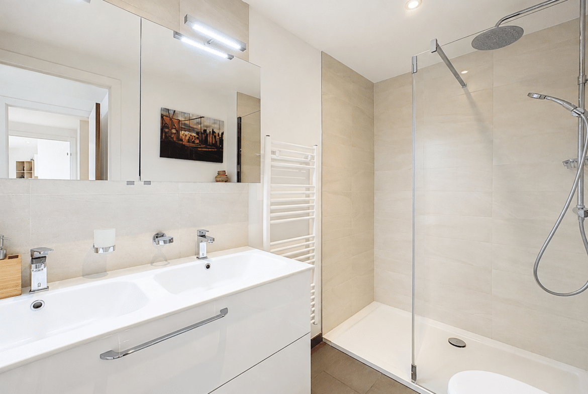Modern bathroom with a white double vanity, large mirror, and a glass-enclosed shower with a rainfall head.