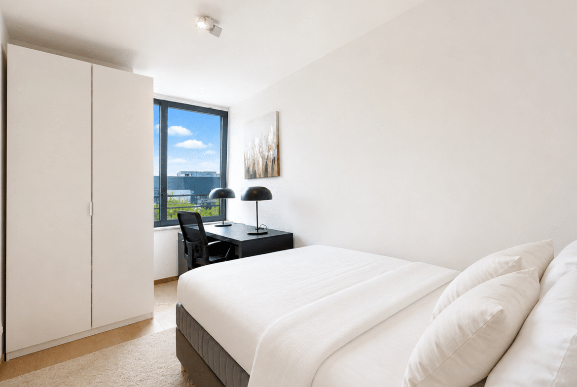 Chambre moderne lumineuse avec bureau, lit blanc et placard intégré dans appartement.