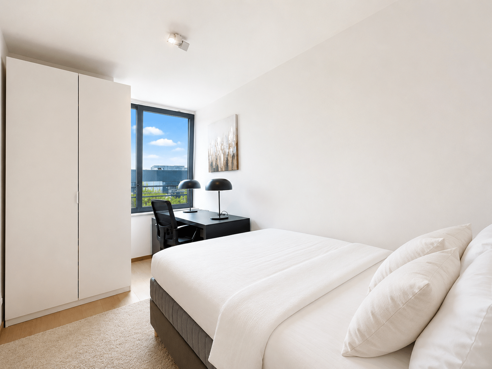 Chambre Moderne Lumineuse – You Real Estate Agency Chambre moderne lumineuse avec bureau, lit blanc et placard intégré dans appartement.