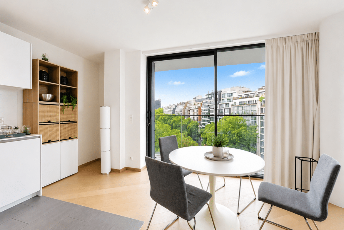 Salle à manger moderne d’appartement avec cuisine ouverte et balcon vue ville.