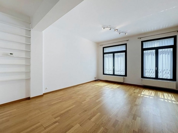 Salon lumineux vide avec parquet grandes fenêtres et étagères intégrées en appartement   appartement 1 chambre  bruxelles