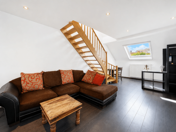 Salon dappartement mansardé lumineux avec escalier en bois et canapé dangle   appartement 1 chambre  ixelles