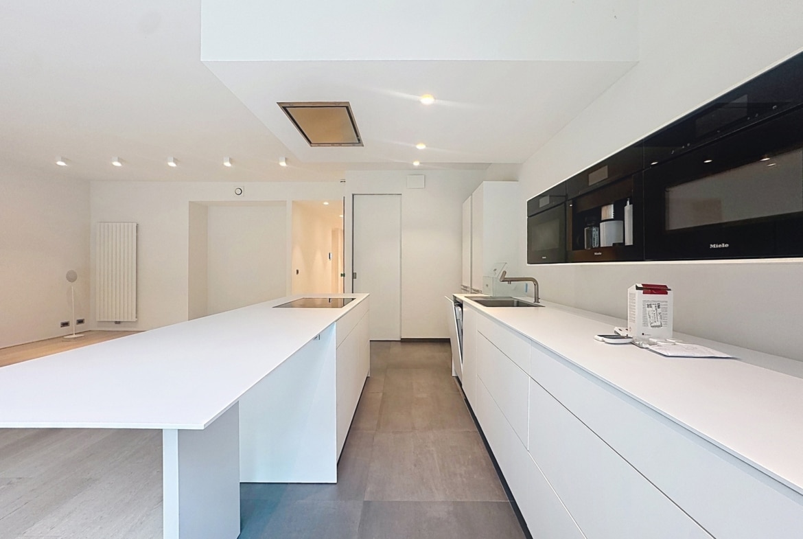 Cuisine ouverte moderne avec îlot central blanc dans appartement contemporain.